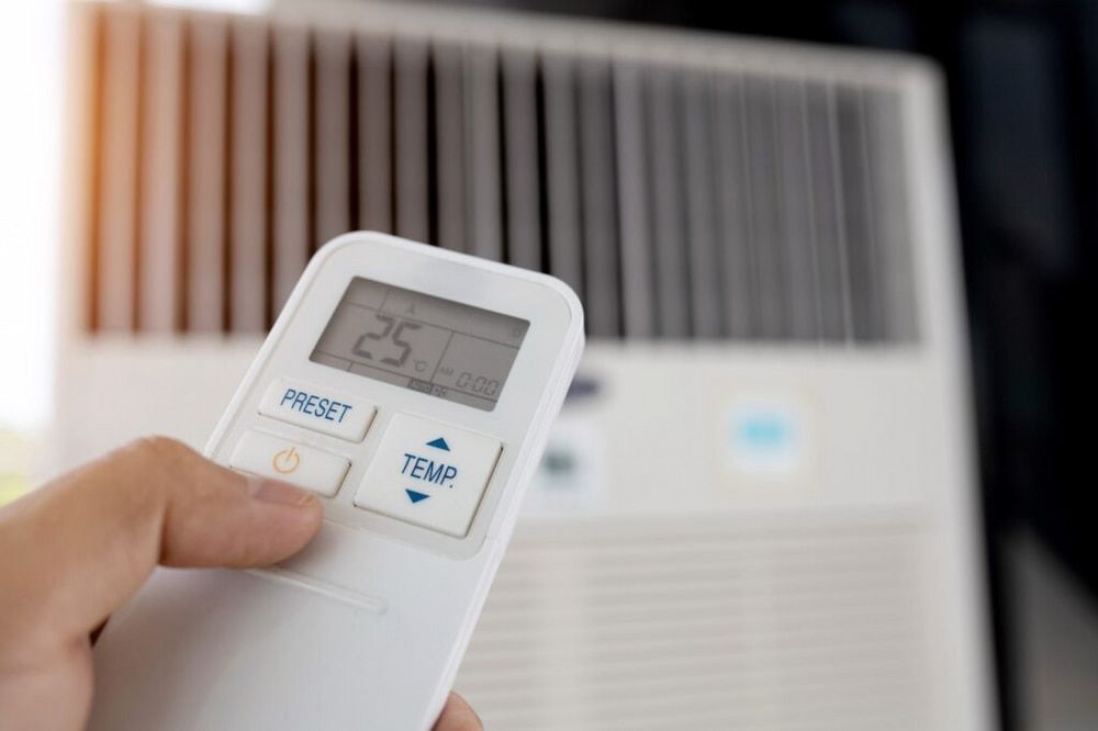 Hand holding an air conditioner remote, pressing the temperature button, with the AC unit in the background. The remote displays a temperature of 25 degrees — Great Northern Airconditioning & Mechanical Services in Berrimah, NT