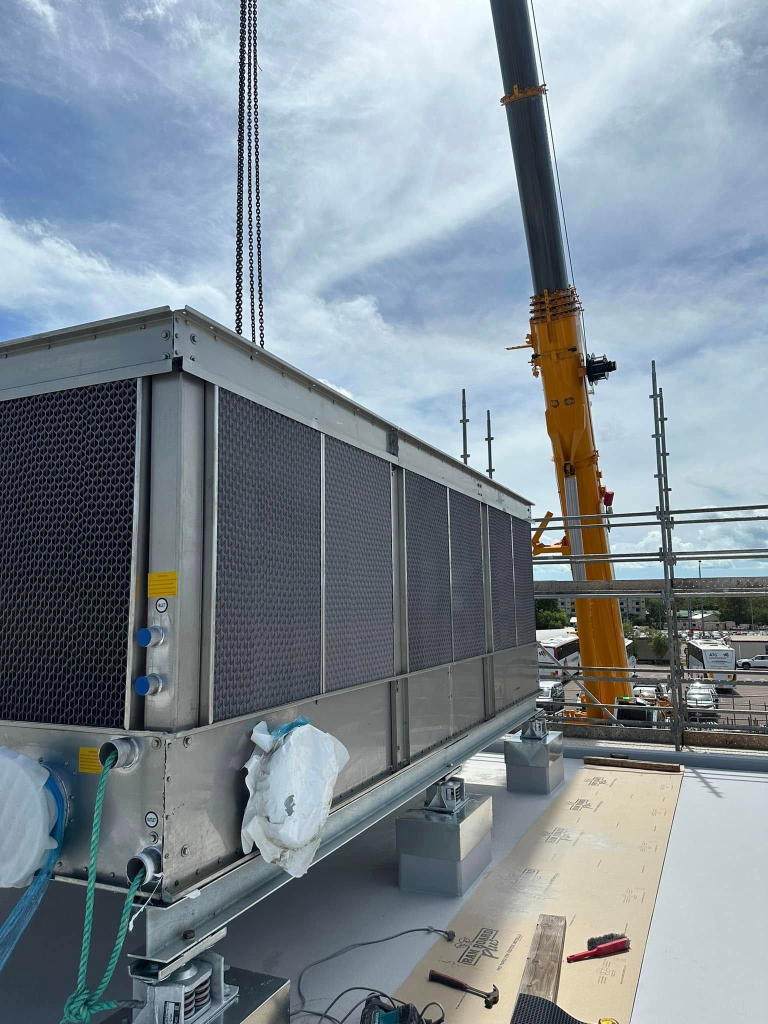 Crane lifting a large air conditioning unit onto a rooftop on a sunny day — Great Northern Airconditioning & Mechanical Services in Berrimah, NT
