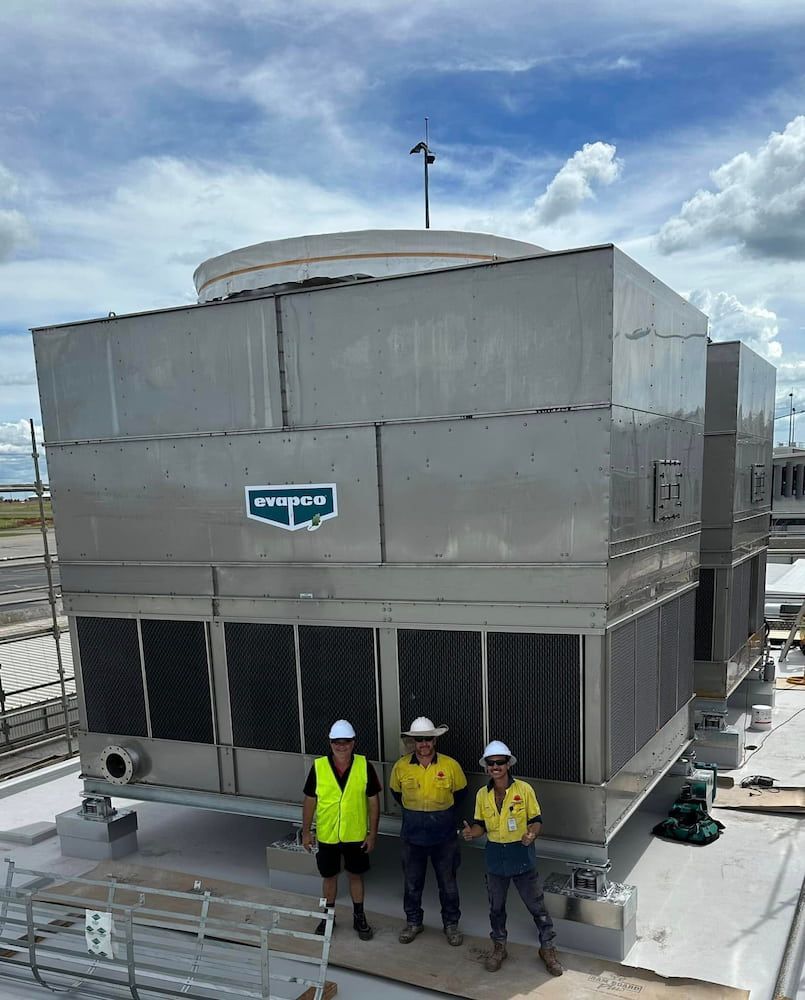 Three Men in Hard Hats and a Large Cooling Tower — Great Northern Airconditioning & Mechanical Services in Berrimah, NT