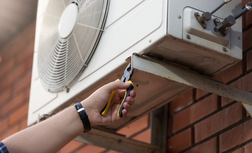 Fixing Aircon on Brick Wall With Pliers — Great Northern Airconditioning & Mechanical Services in Howard Springs, NT