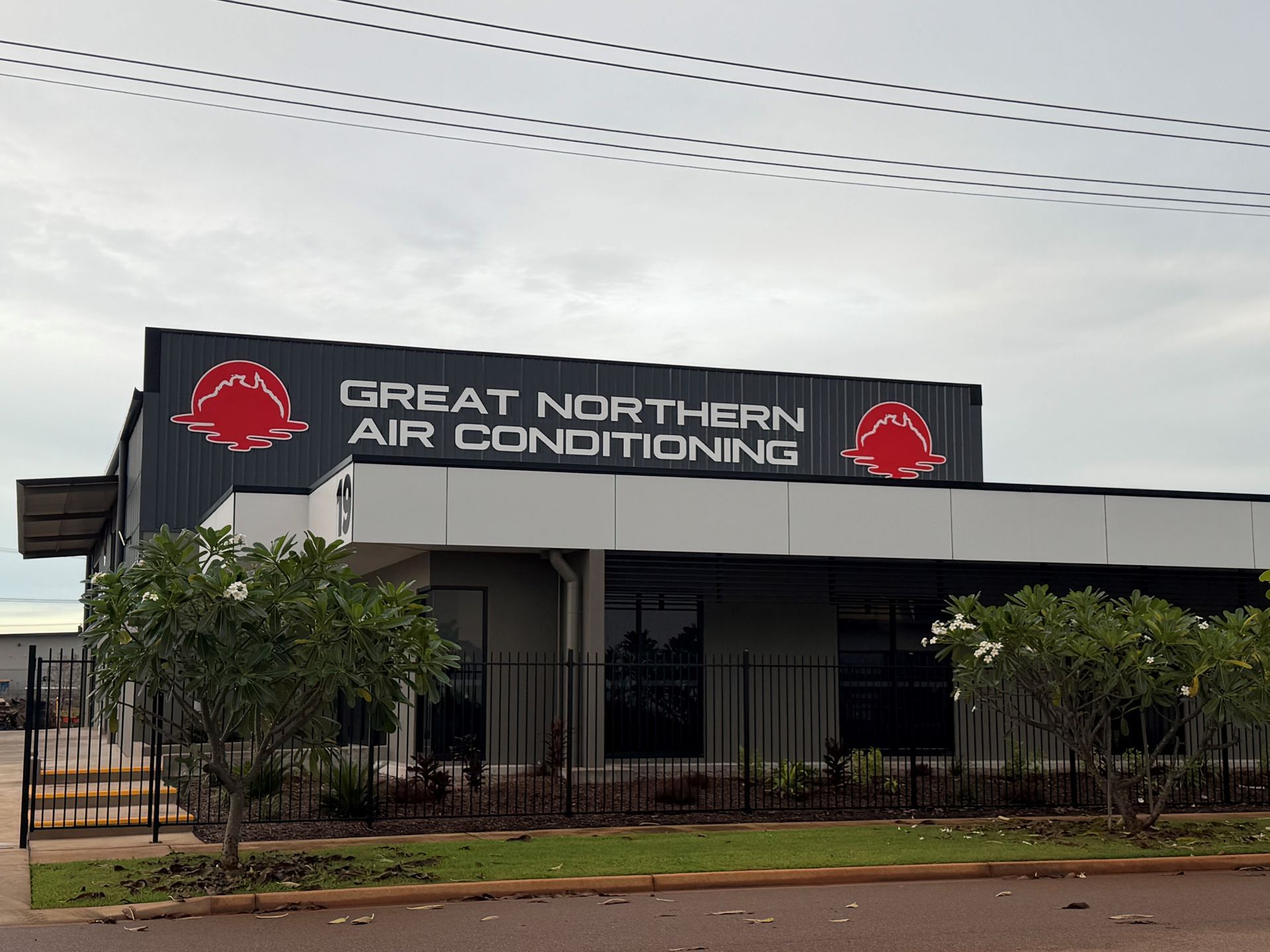 Great Northern Air Conditioning building with a red and grey logo on a cloudy day — Great Northern Airconditioning & Mechanical Services in Berrimah, NT