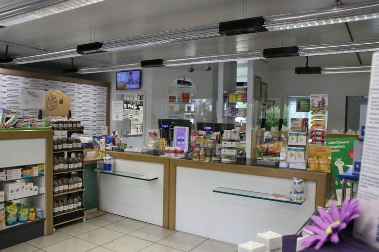 Innenansicht einer Apotheke mit Theke, Regalen voller Produkte und einem Fernsehbildschirm.