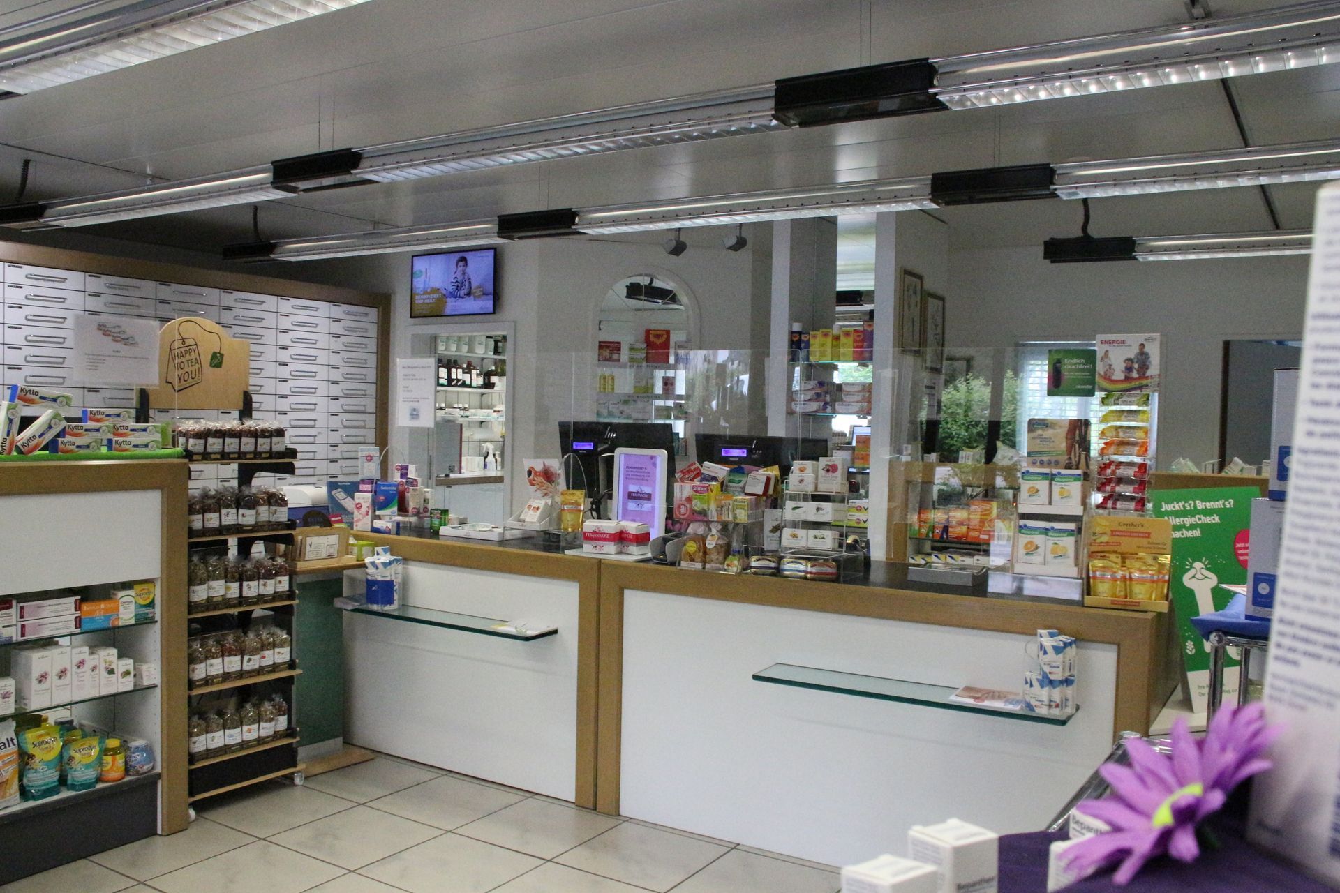 Innenaufnahme einer Apotheke mit Theke und ausgestellten Produkten. Farbgestaltung in Weiss und Braun.