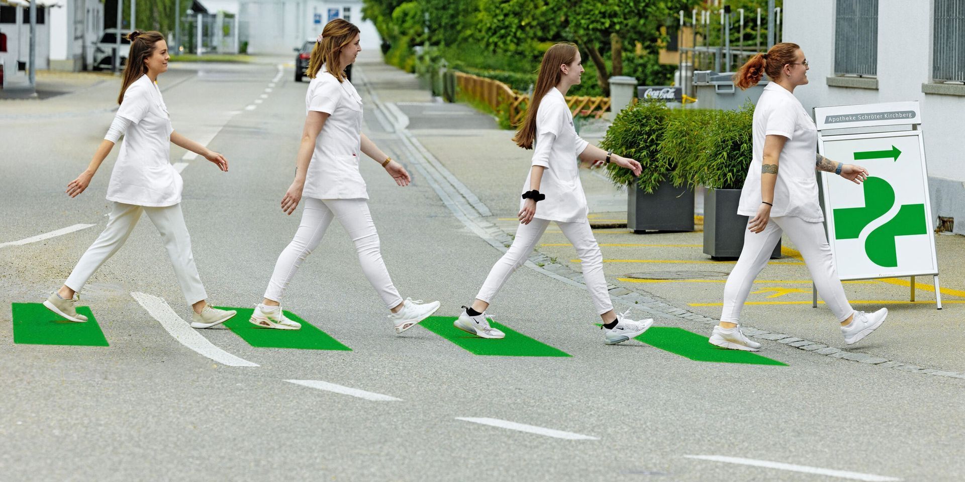Vier Personen in weissen Outfits überqueren eine Strasse auf grün bemalten Quadraten und ahmen damit das Cover des Beatles-Albums Abbey Road nach.