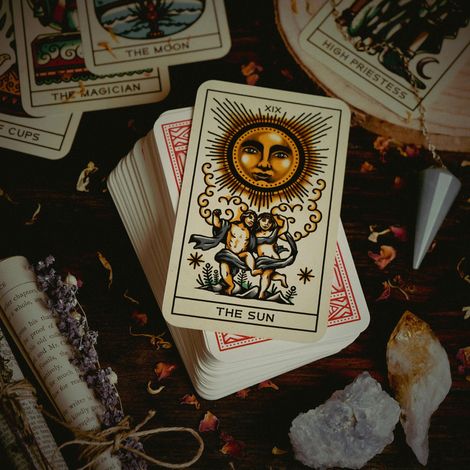 Tarot cards spread on a dark table, with The Sun card centered among crystals and herbs.