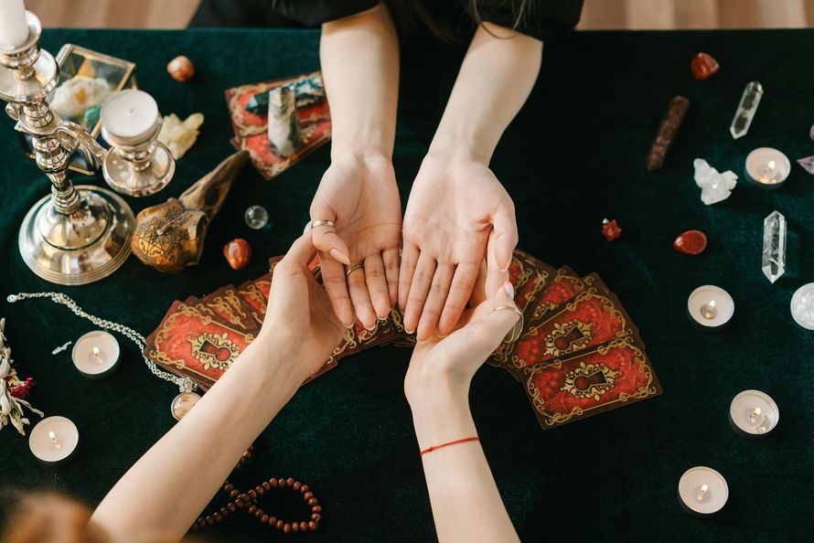 Hands held over a colorful patterned cloth with candles and crystals on a dark table