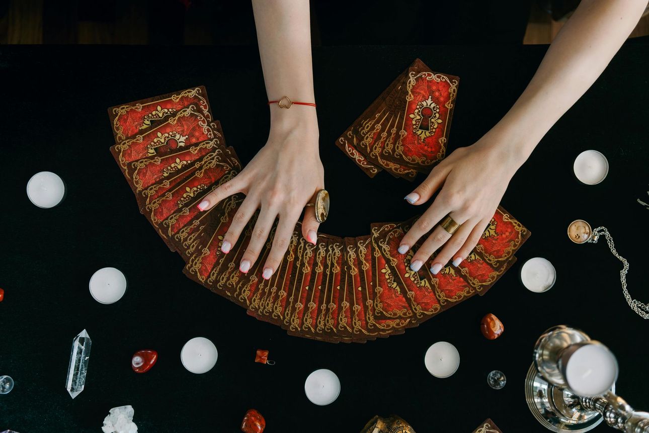 Hands arranging a red-and-gold fan of cards on a black tabletop with scattered trinkets