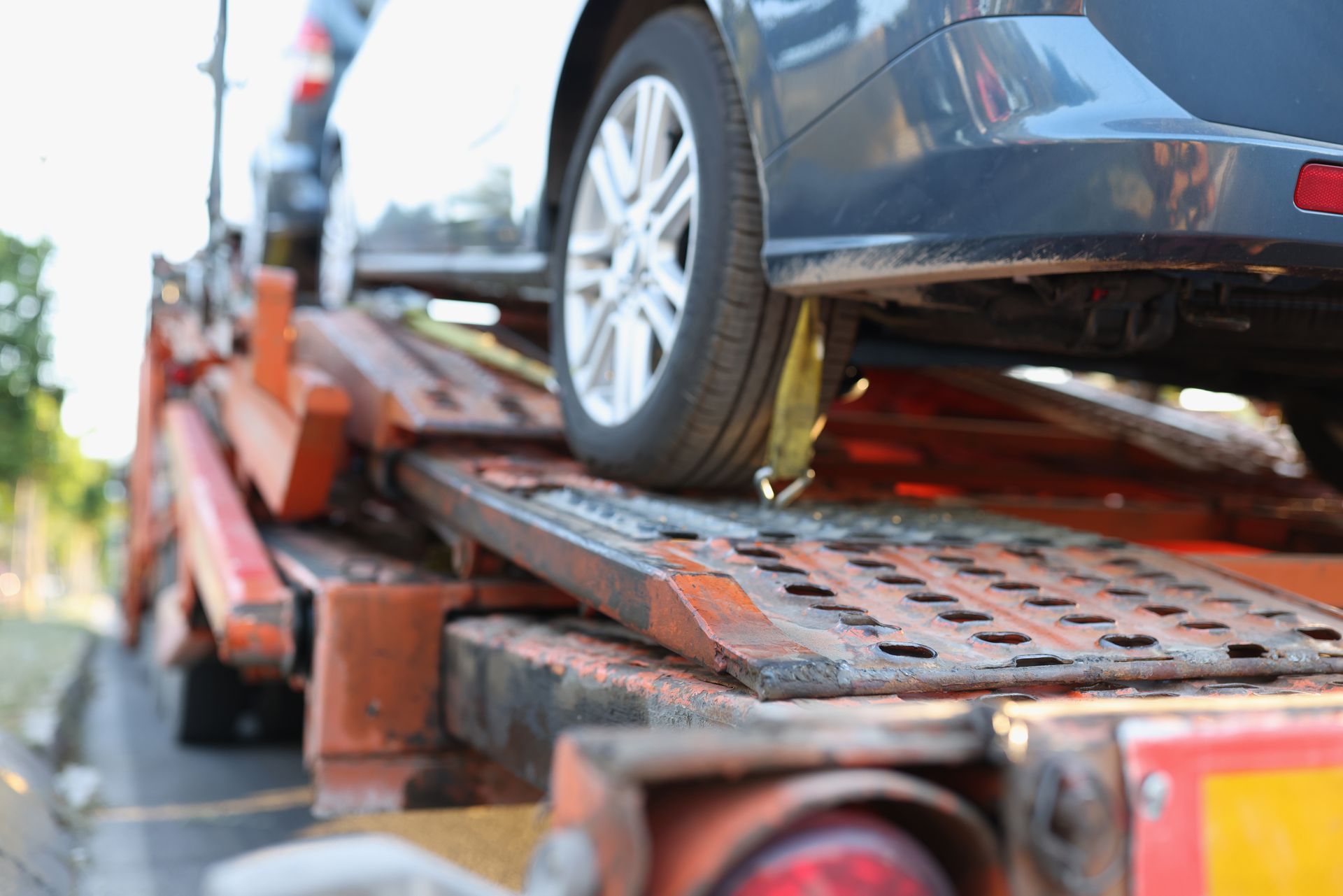 Car being loaded onto a rusty car carrier trailer. Gray car tire on a metal ramp.
