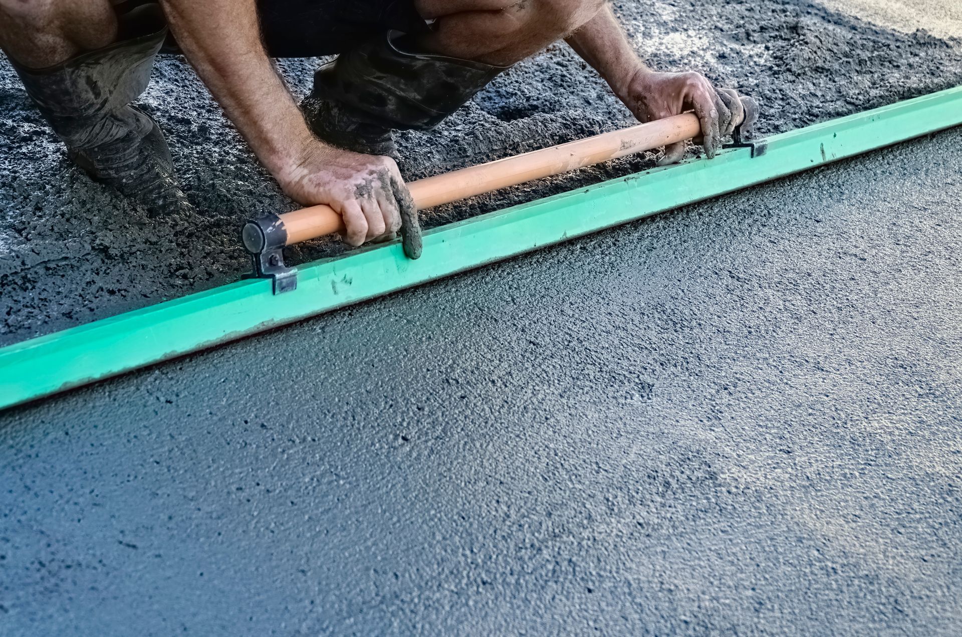 A concrete driveway contractor smoothing freshly poured driveway concrete with a float.