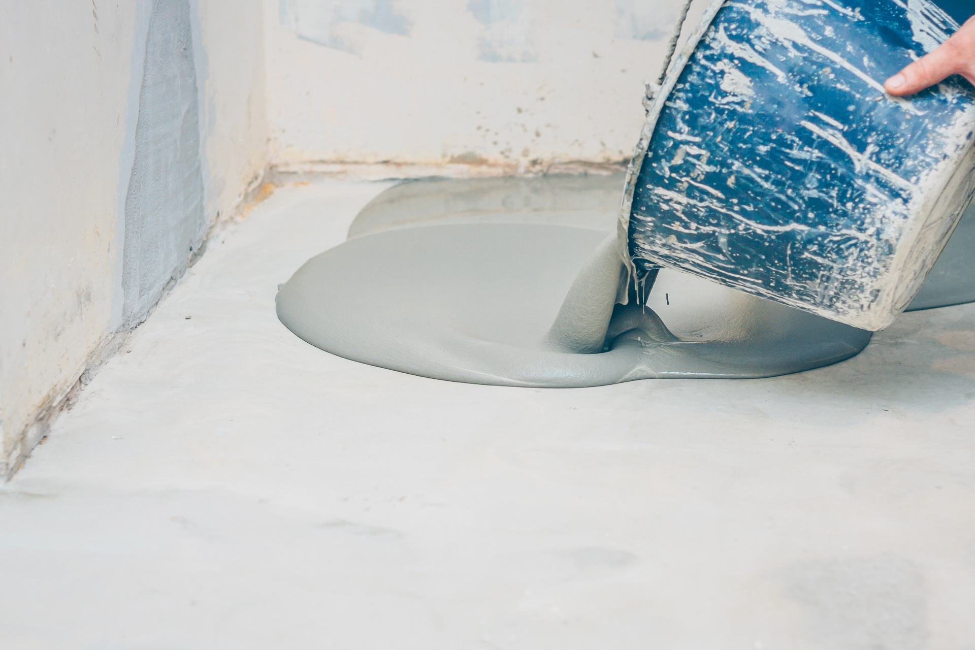 Pouring self-leveling concrete onto a floor to create a smooth, even subfloor surface.