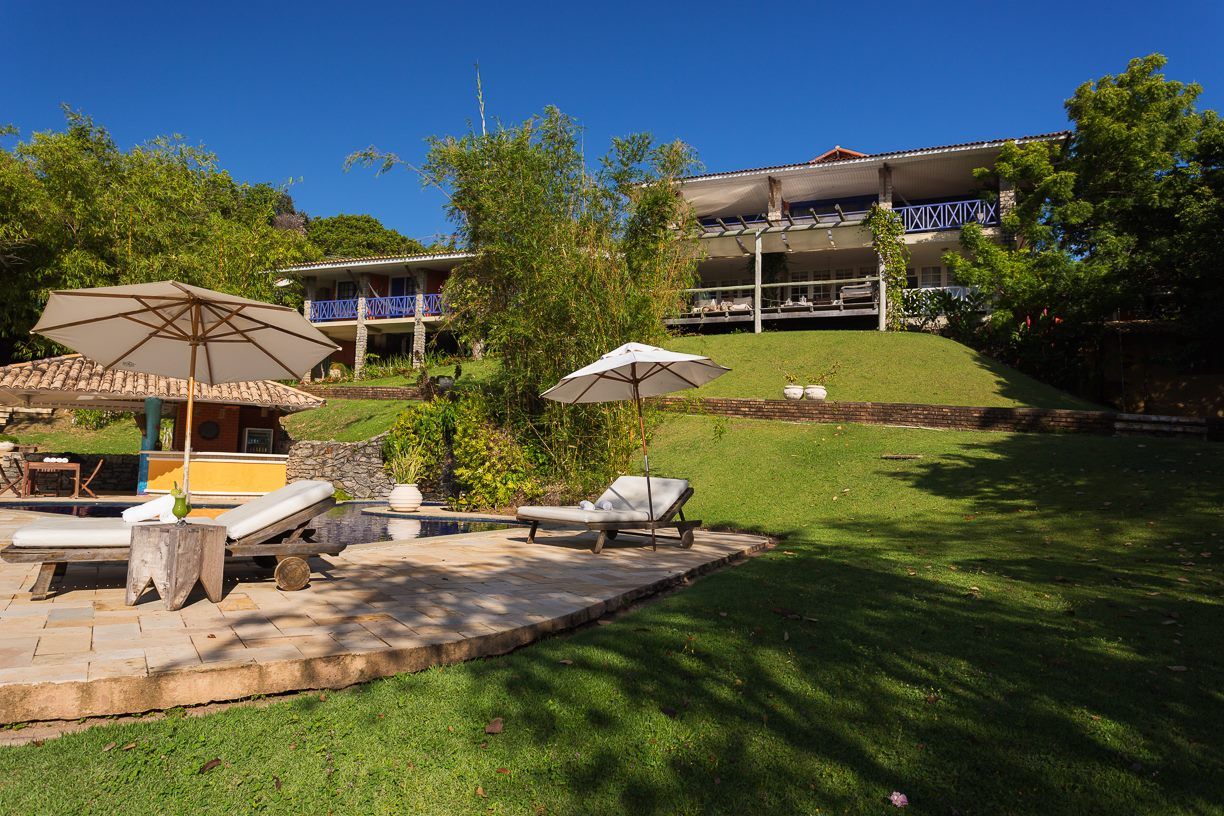Uma casa grande está situada no topo de uma colina no meio de um campo verdejante.