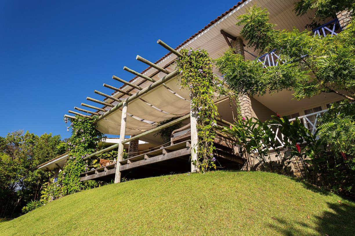 Uma casa com uma pérgola no topo de uma colina gramada.
