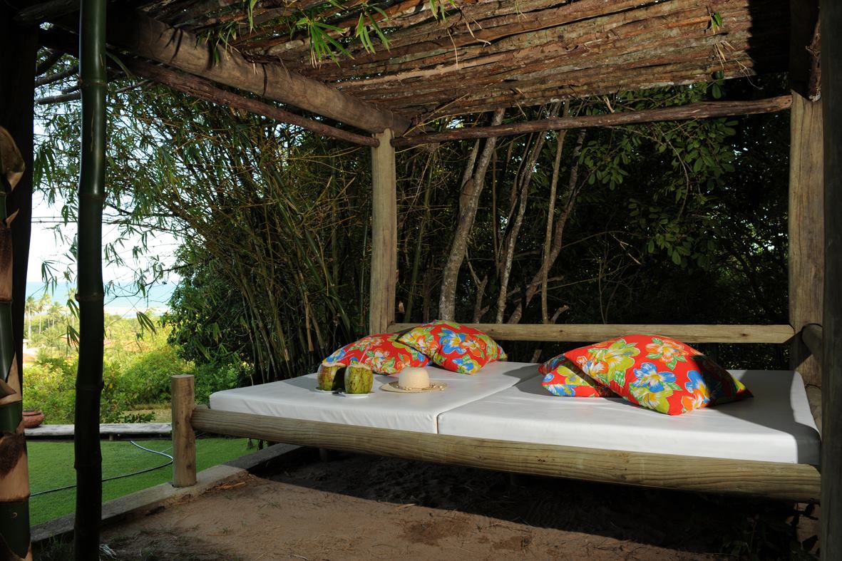 Uma cama de madeira com almofadas coloridas sob um dossel na floresta.