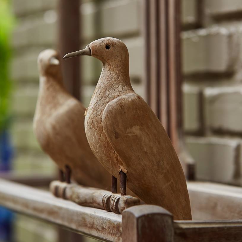 Dois pássaros de madeira estão sentados em um corrimão de madeira.