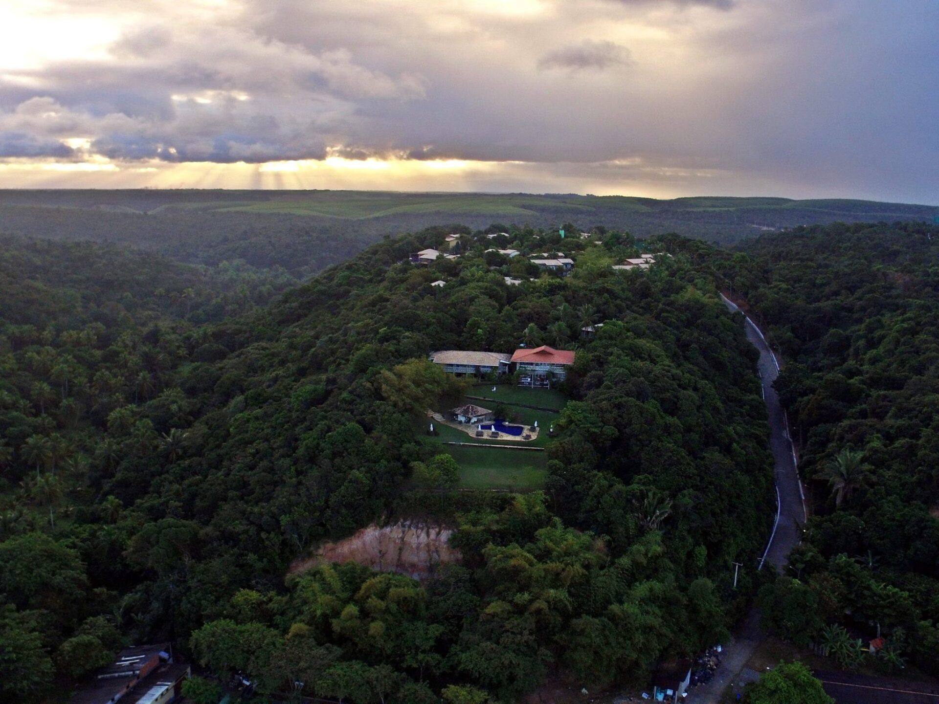 Uma vista aérea de uma casa no topo de uma colina cercada por árvores.