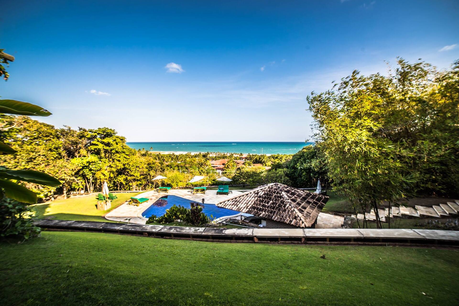 Há uma grande piscina no meio de um campo verdejante com vista para o oceano.