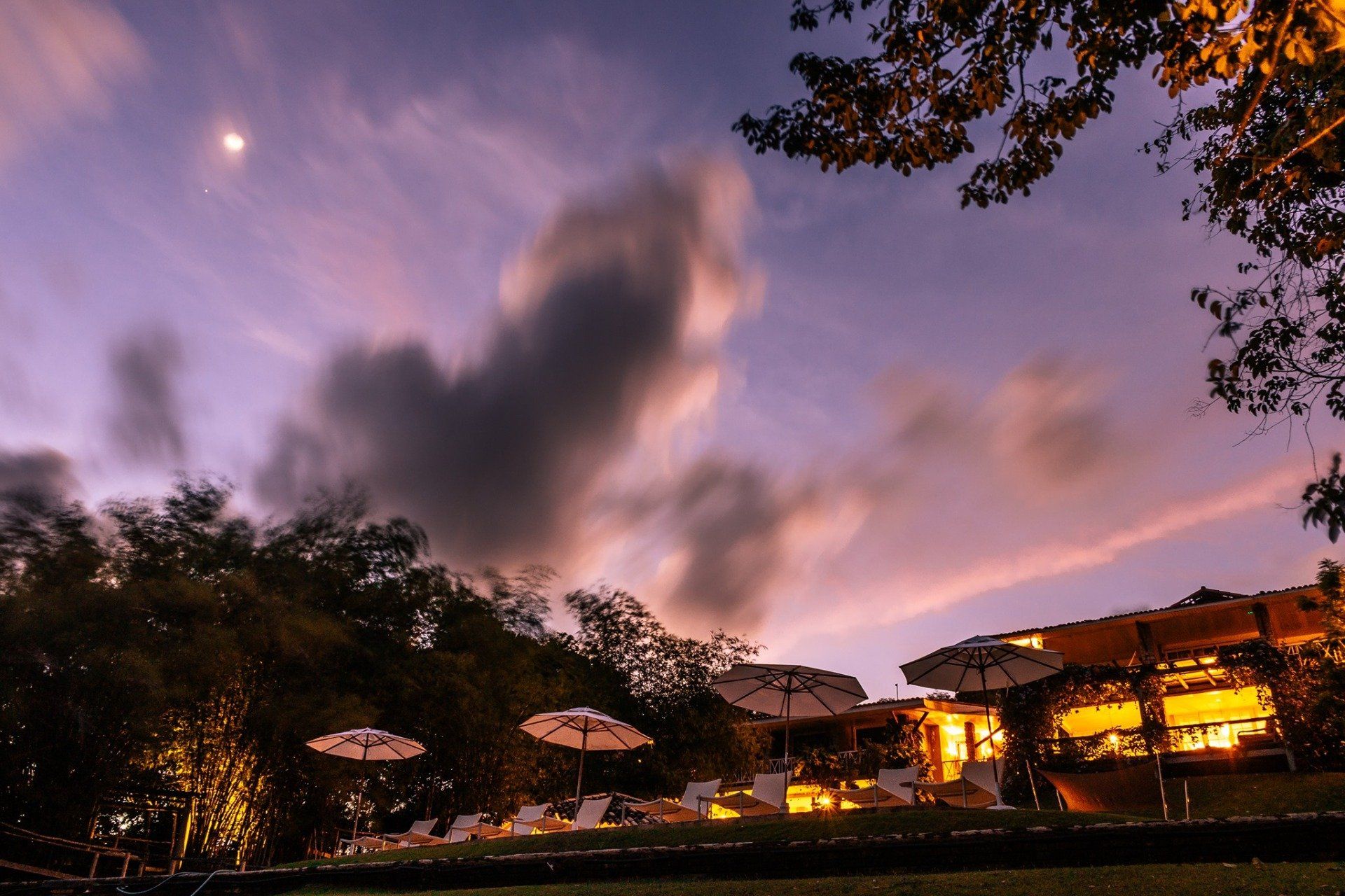 Um pôr do sol sobre uma piscina com guarda-sóis e cadeiras