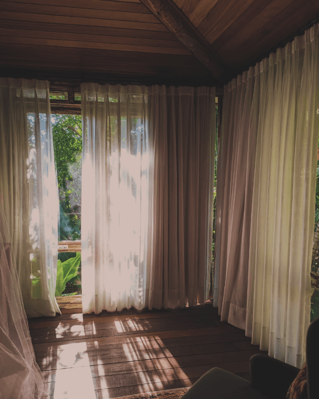 O sol está brilhando através das cortinas de uma sala com piso de madeira.