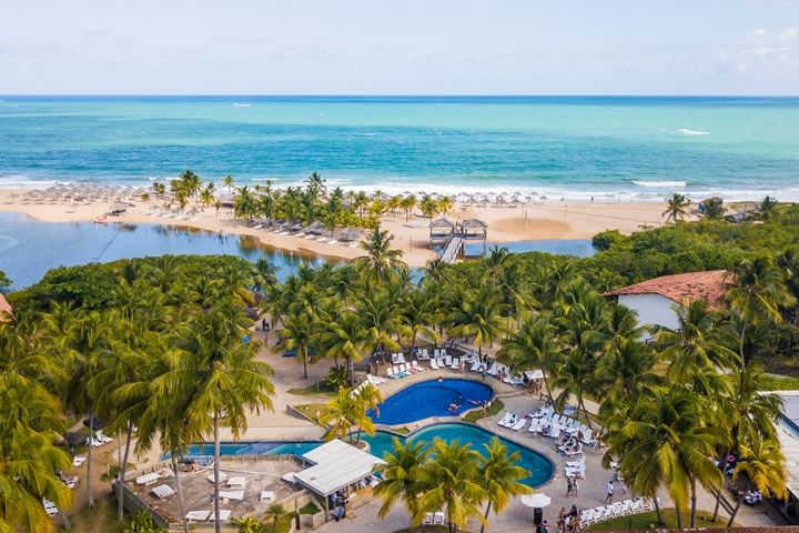 Uma vista aérea de um resort tropical com palmeiras e uma grande piscina.