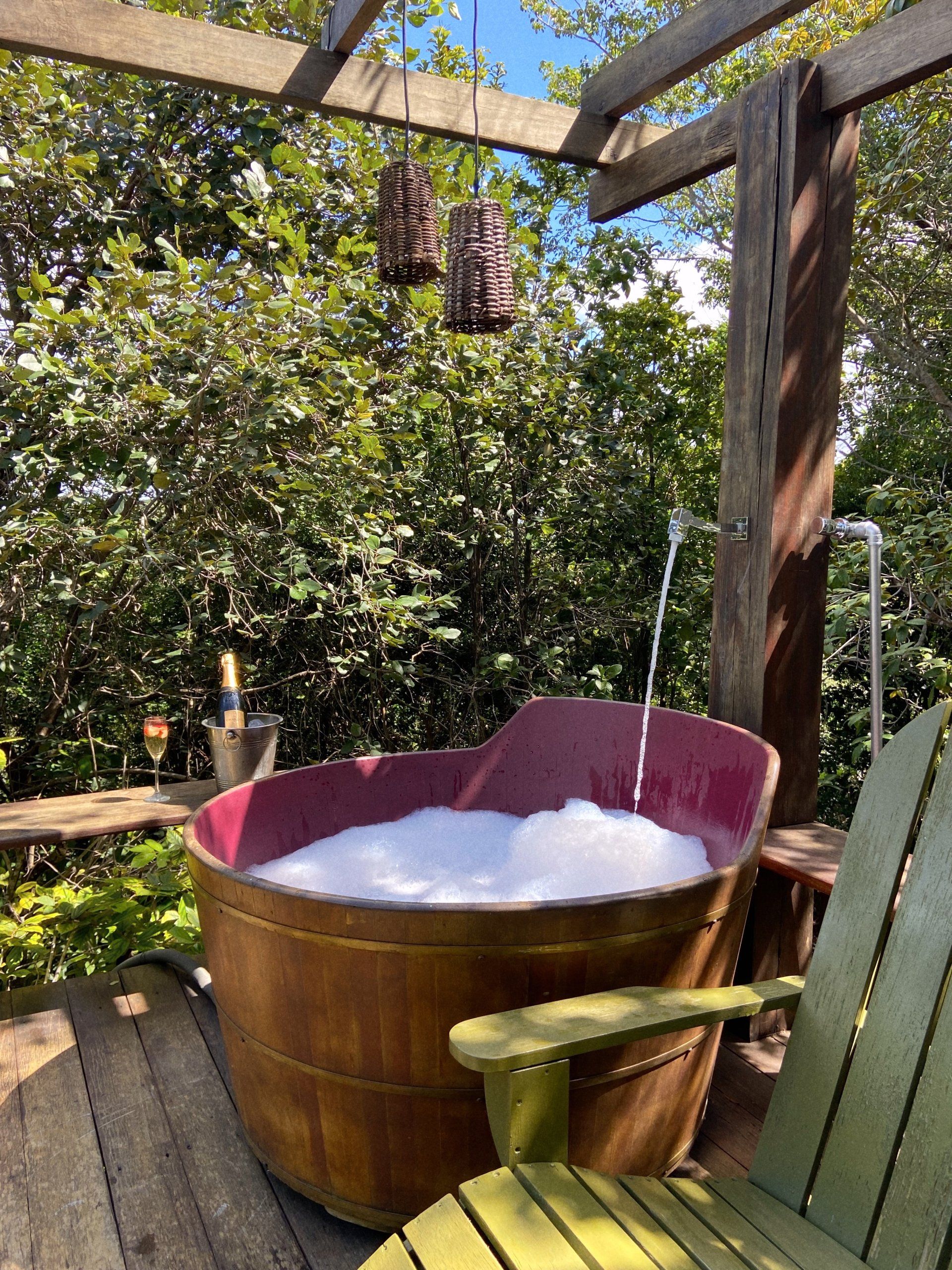 Uma banheira de madeira cheia de espuma está no convés ao lado de uma cadeira.