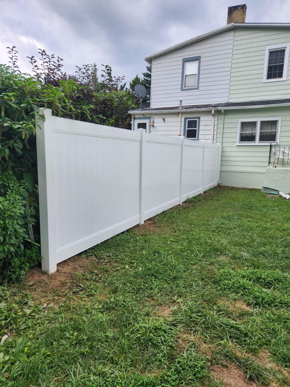 White vinyl fence borders a grassy backyard, adjacent to a light green house. White vinyl fence borders a grassy backyard, adjacent to a light green house.