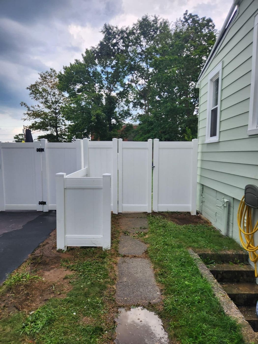 White vinyl fence and gate next to a house with a concrete walkway.