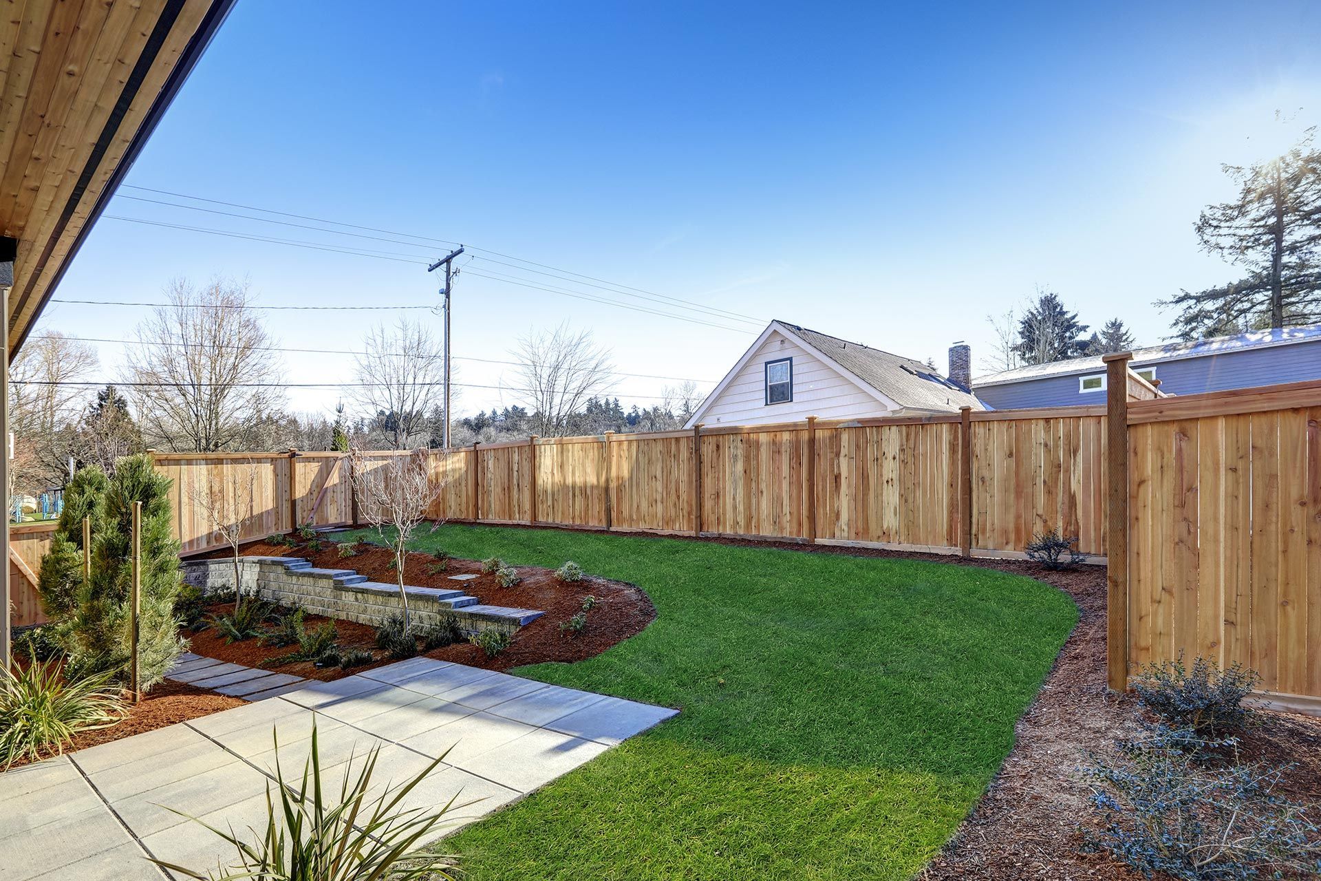 Well-maintained backyard with wooden fence, green lawn, flower beds, and blue sky. Well-maintained backyard with wooden fence, green lawn, flower beds, and blue sky.