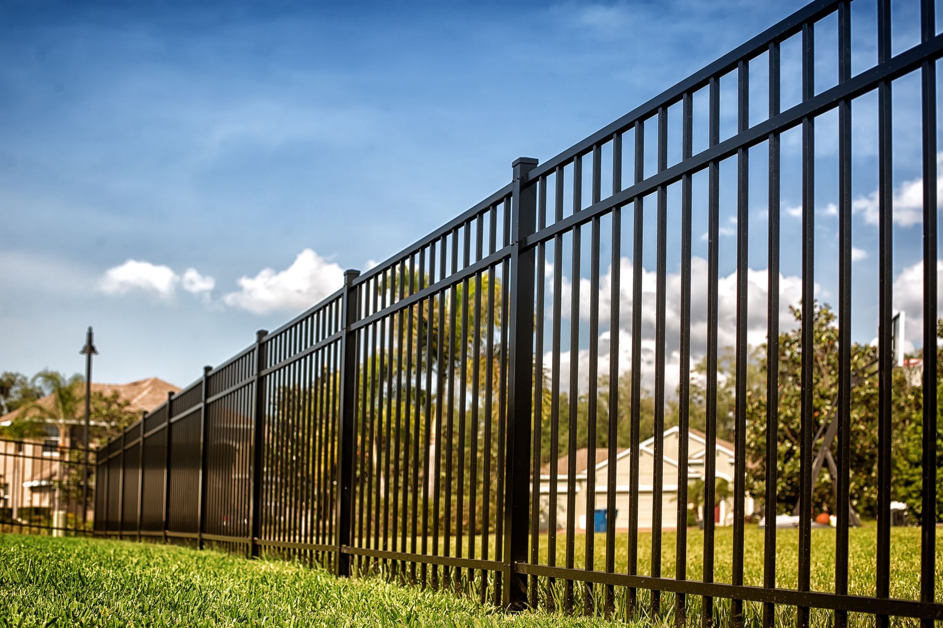 A black metal picket fence stretching across a green lawn under a partly cloudy sky.