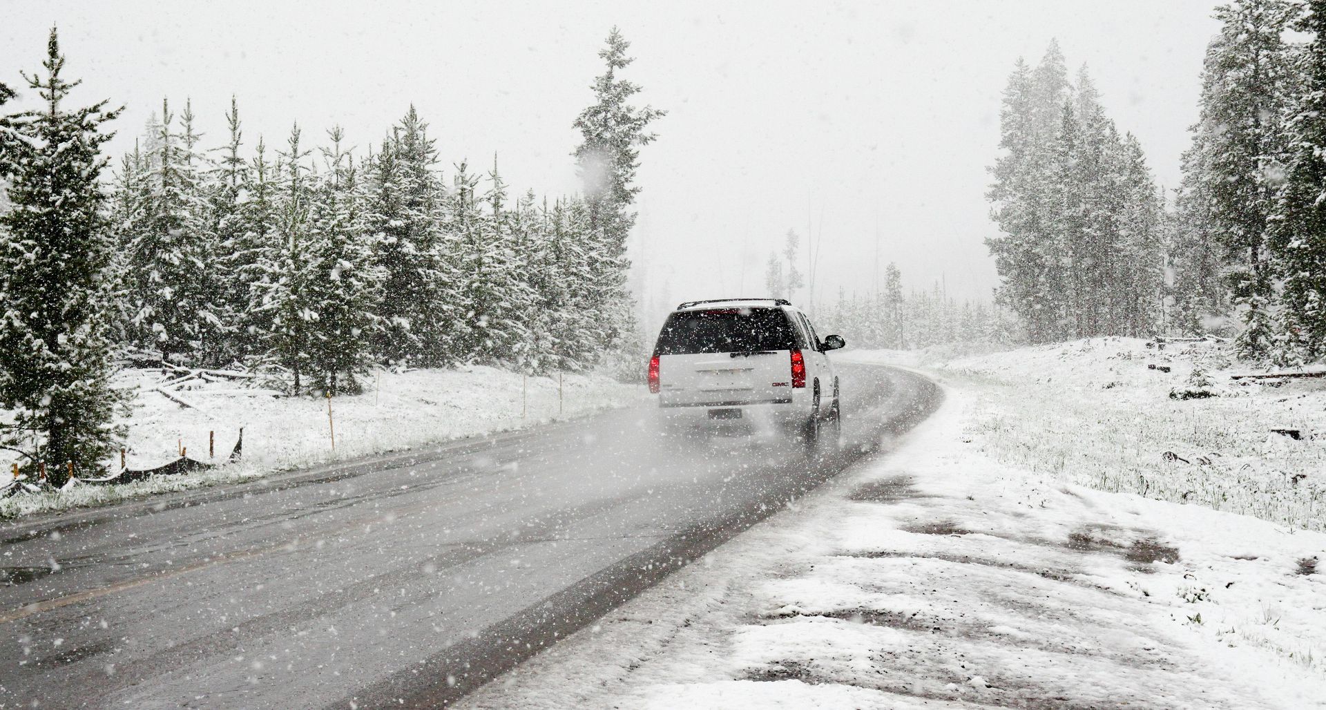 SUV driving on snowy road through a forest; white snow covers trees and ground.