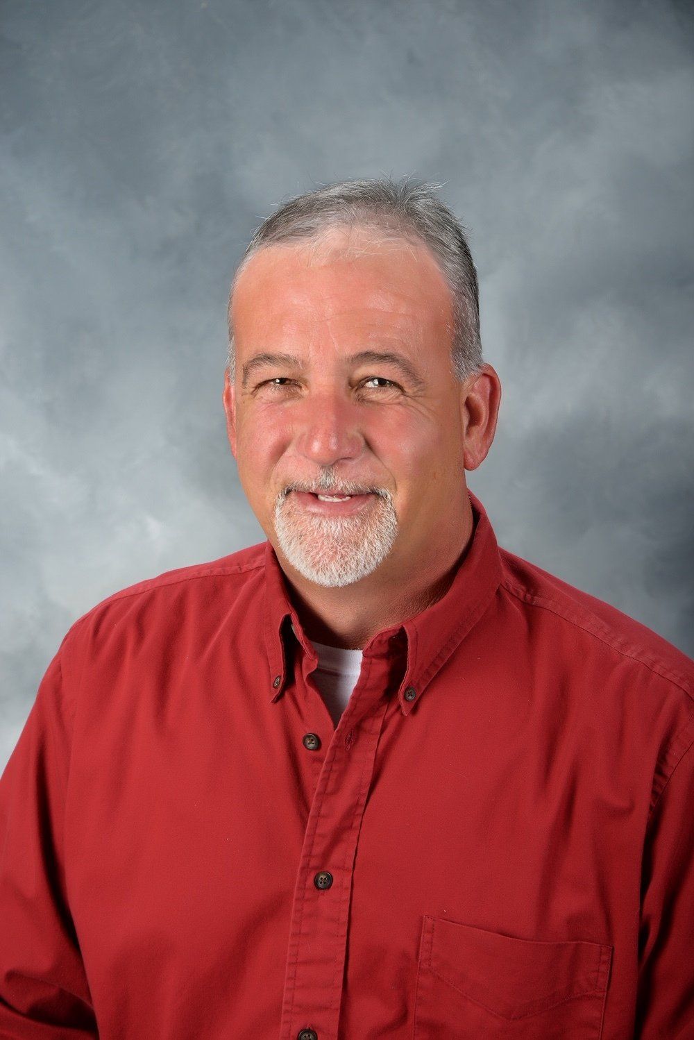 A man with a beard is wearing a red shirt and smiling for the camera.