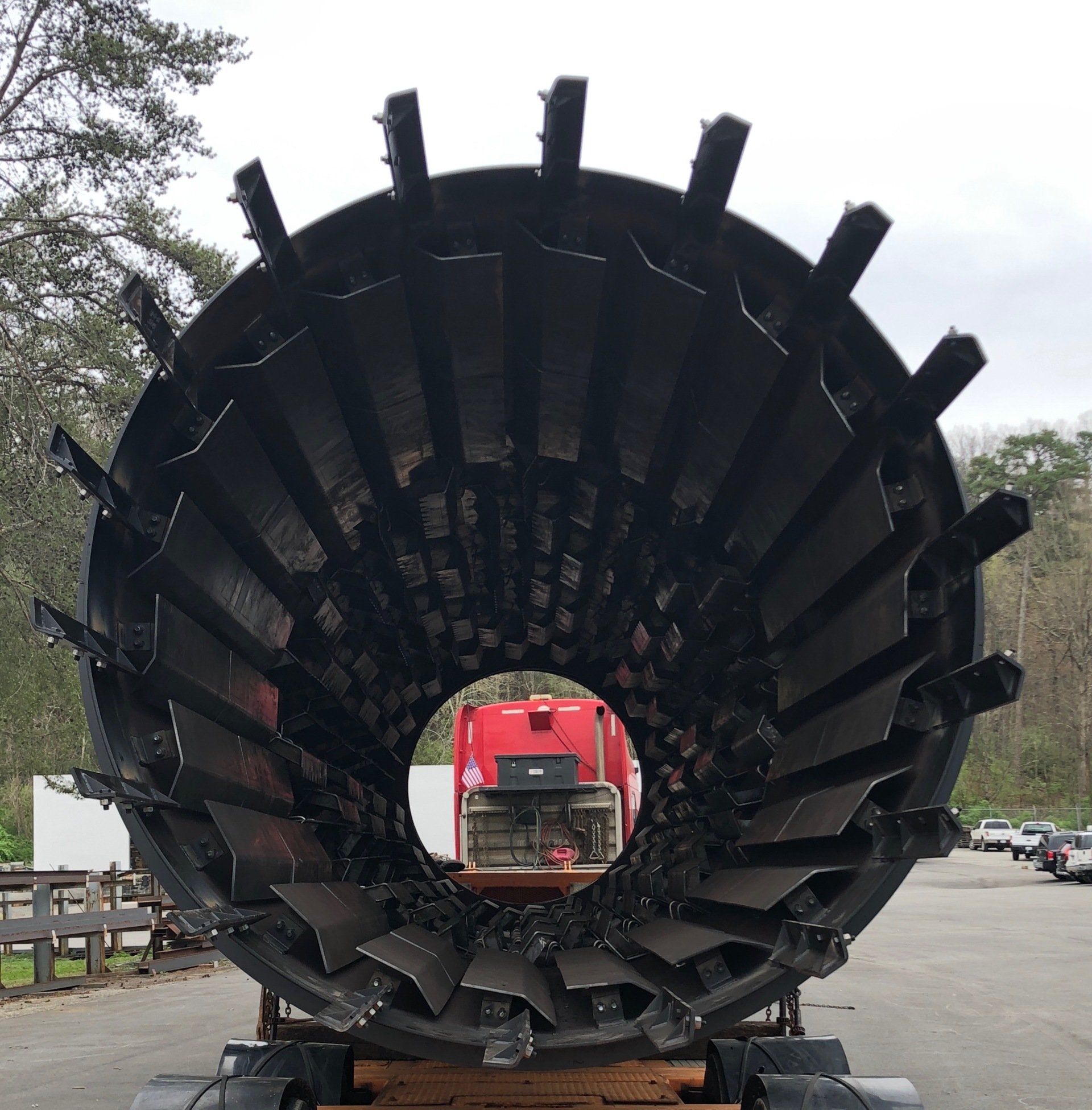 A large metal object is sitting in a parking lot next to a red truck