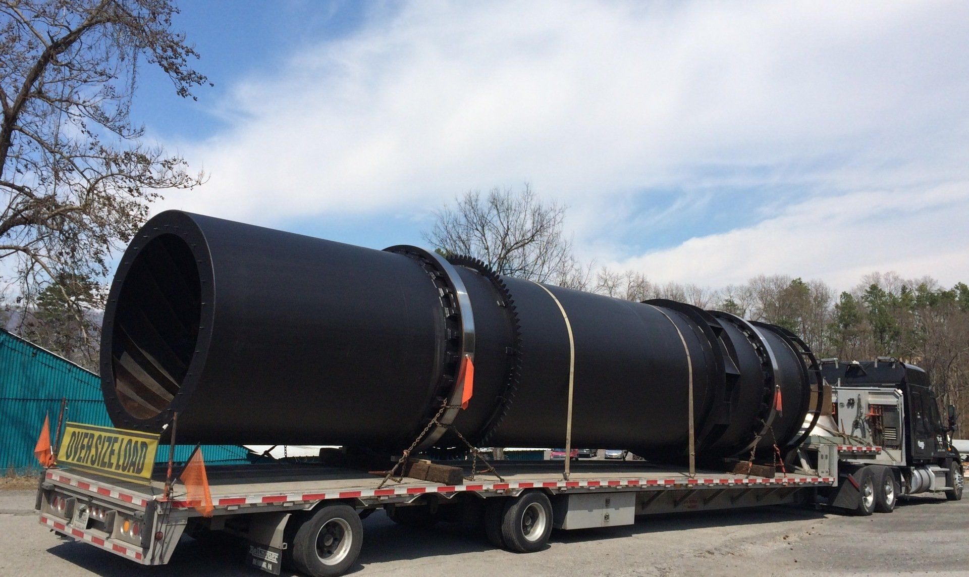 A large black pipe is being transported on a semi truck.