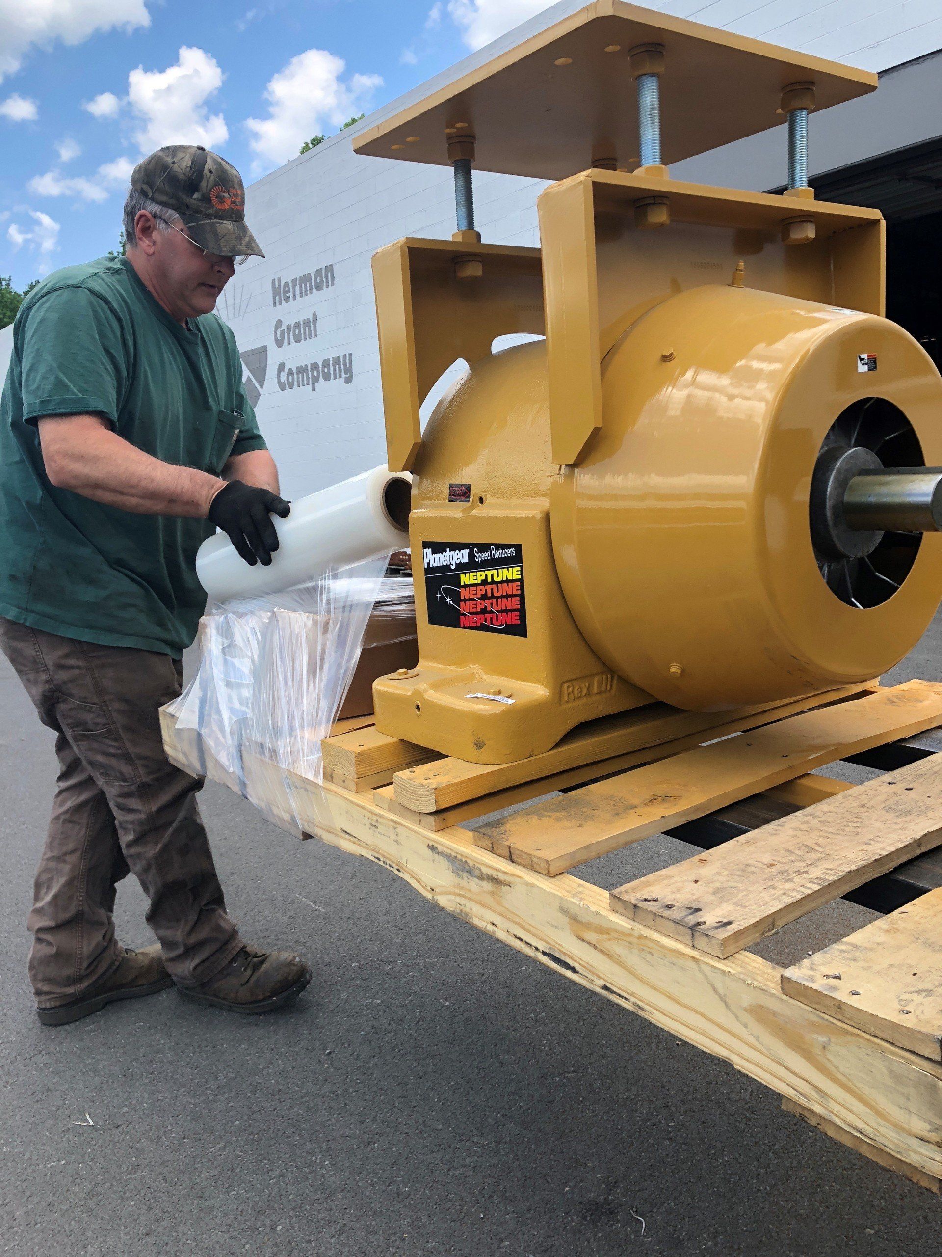 A man is standing next to a large yellow machine on a wooden pallet.