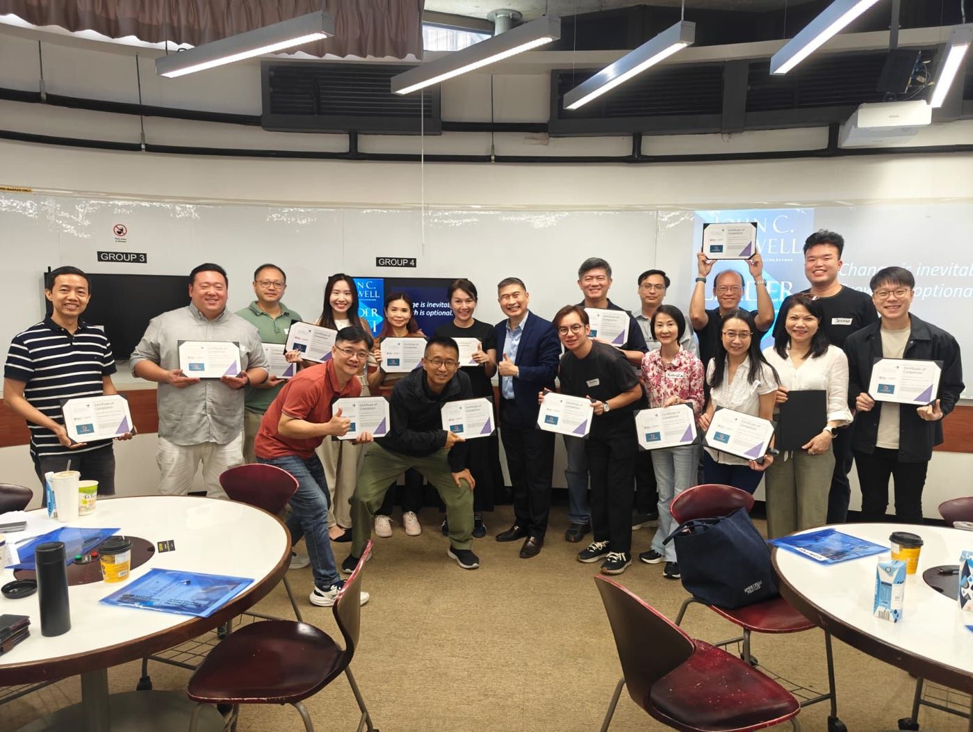 A group of people holding certificates, posing for a photo in a brightly lit room. They appear to be celebrating a professional accomplishment.