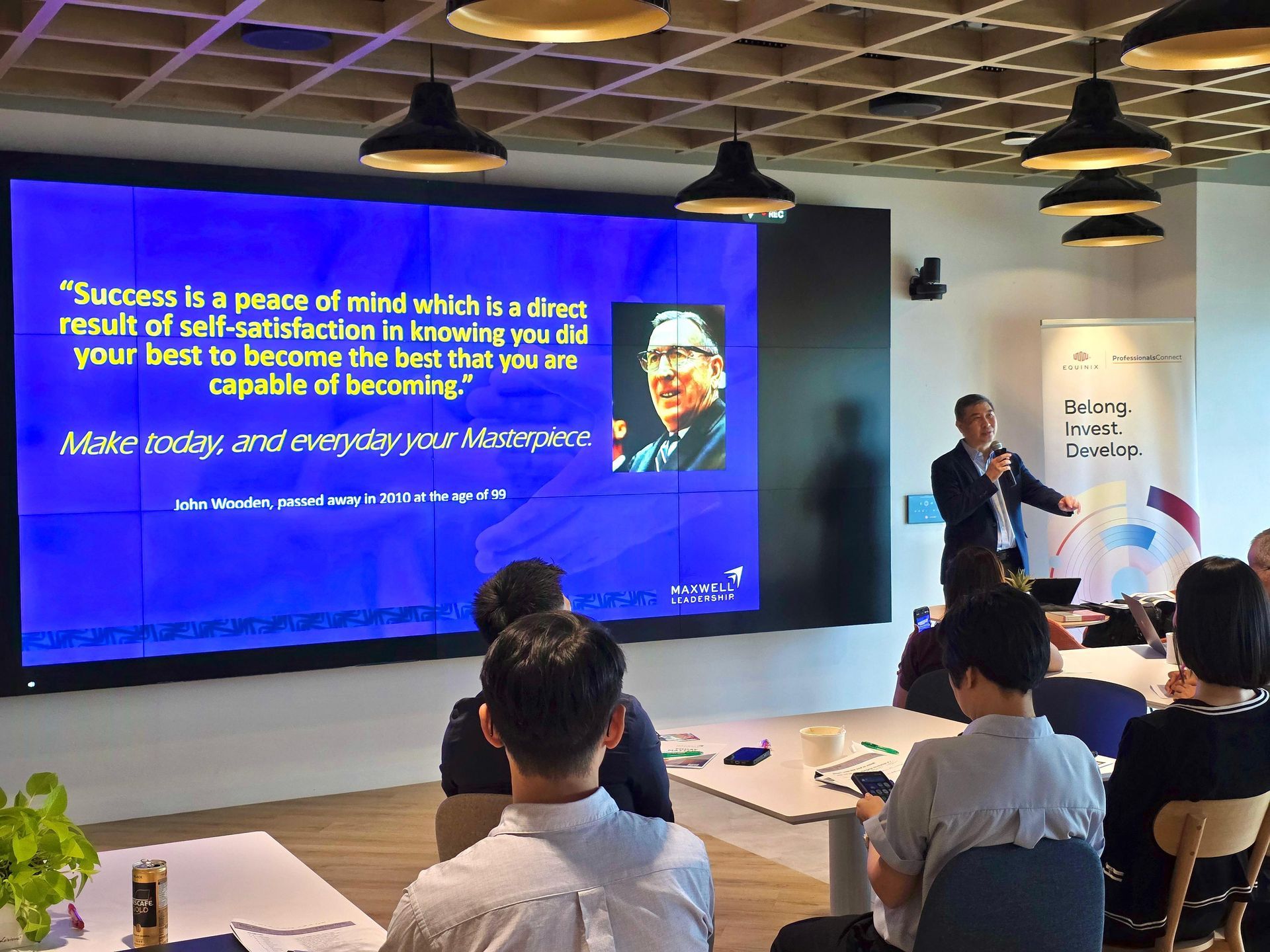 A man giving a presentation in front of a screen with a quote and a picture. Several people are in the audience.