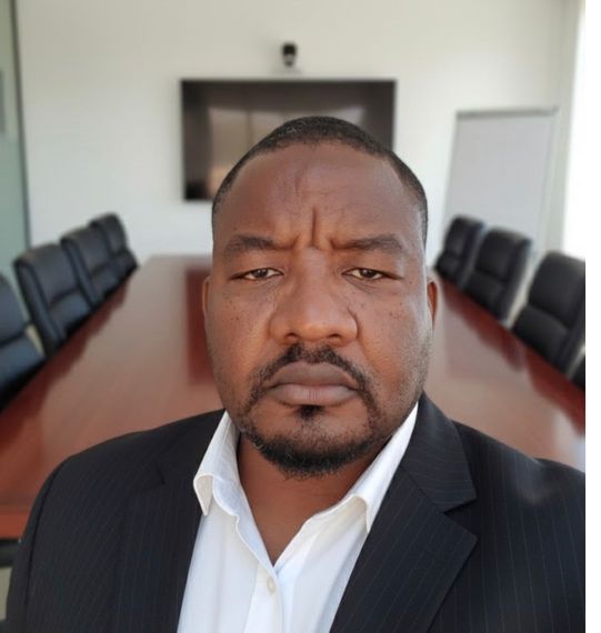 Man in a suit in a boardroom, with a serious expression, looking directly at the viewer.