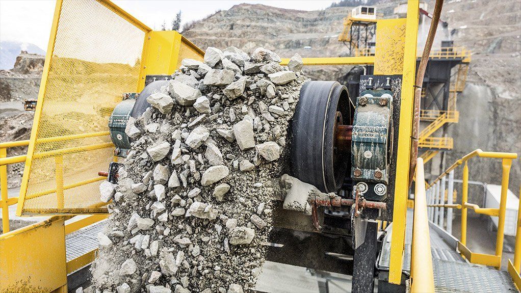 Yellow industrial rock crusher processing stone in outdoor setting. Dust visible.