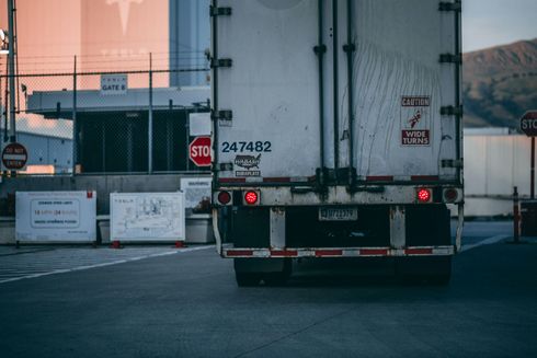 Rear view of a semi-truck with tail lights on, stopped near a security checkpoint.