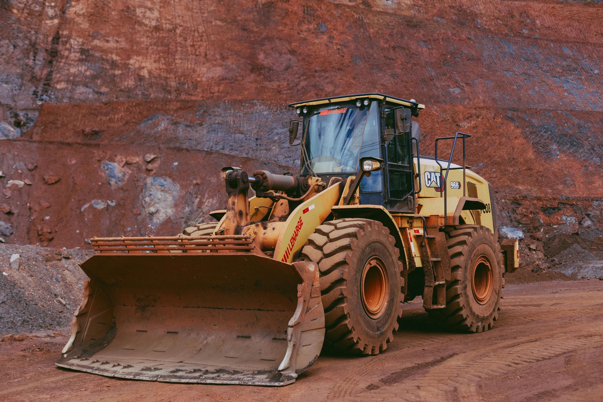 Yellow front-end loader in a quarry with a red rock face.