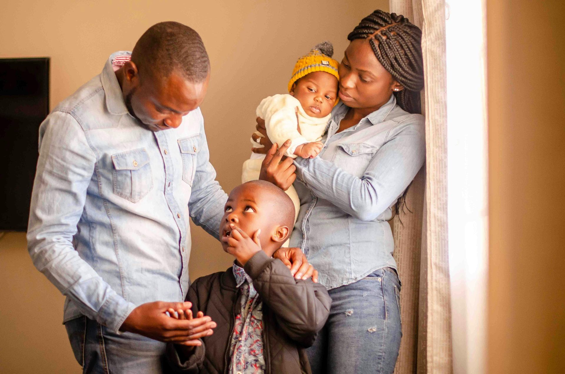 Family poses together; mom holds baby, dad and older child look at them indoors.