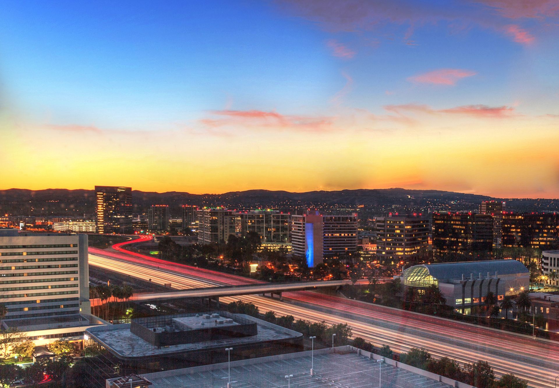 City skyline at sunset with a highway illuminated by car lights. Blue, orange and yellow sky.