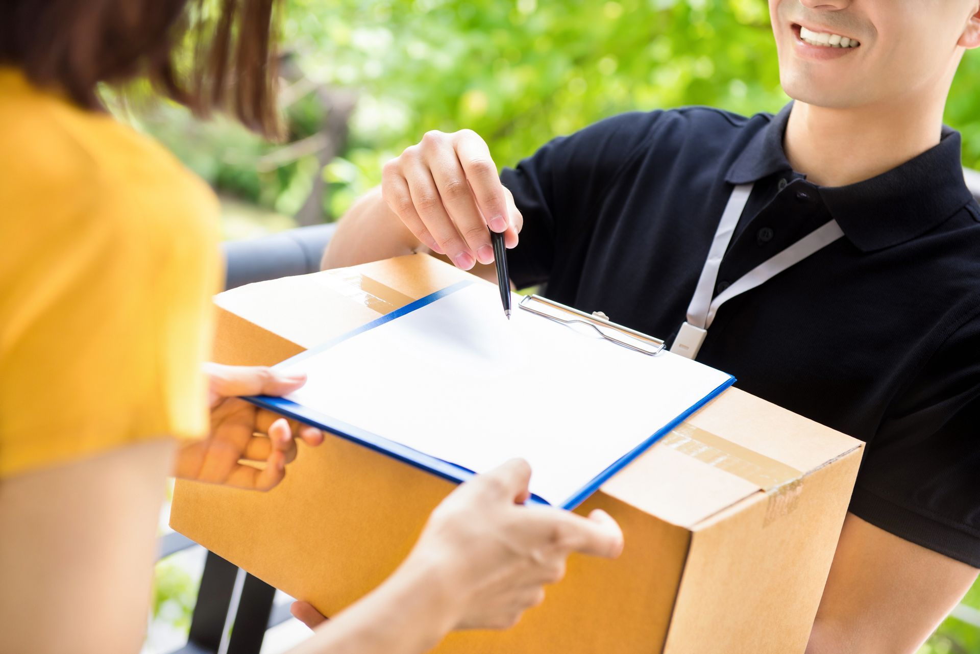 Delivery person handing a cardboard box to a person, holding a clipboard for signature.