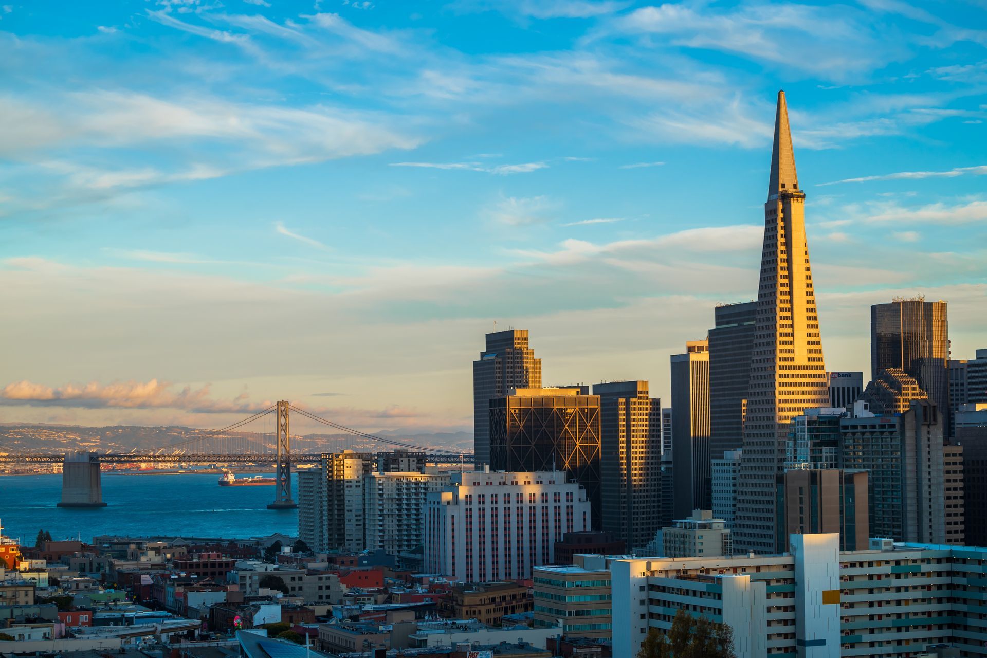 San Francisco skyline with Transamerica Pyramid, blue sky, water, and Golden Gate Bridge.