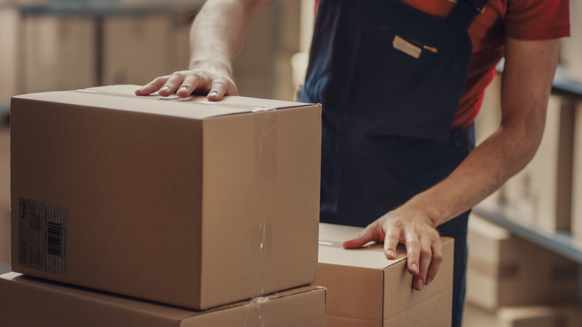 Person in overalls stacking cardboard boxes in a warehouse.