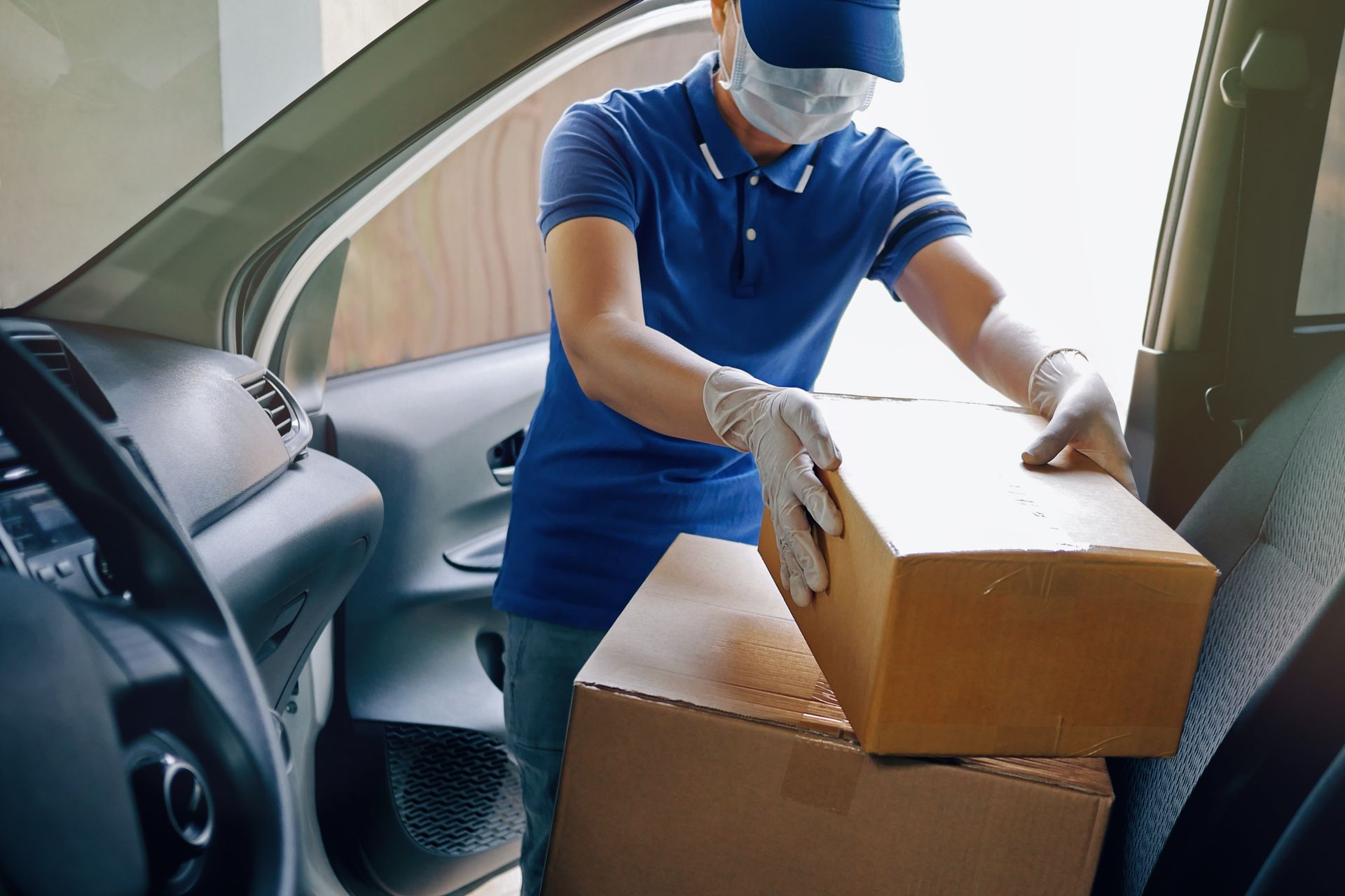 Delivery person wearing mask and gloves loads packages into a car.