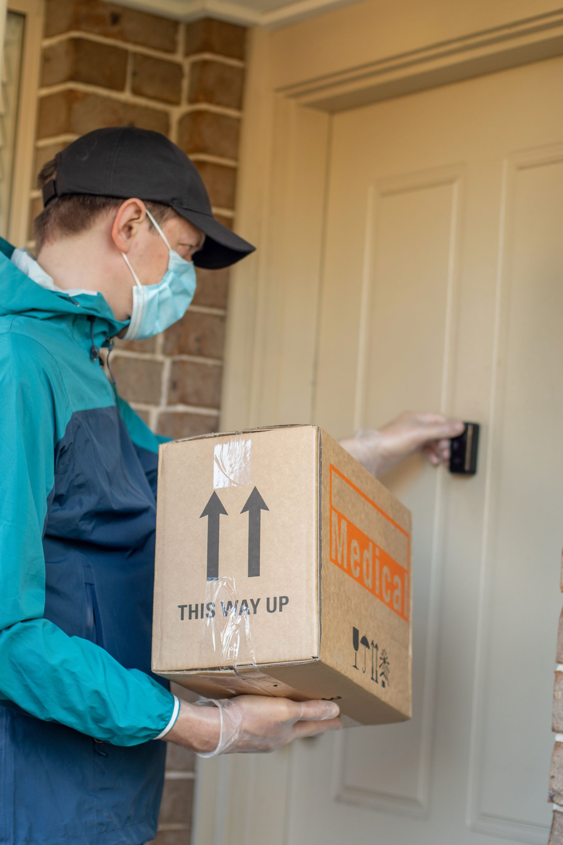 Delivery person wearing mask and gloves rings doorbell, holding a cardboard box with 