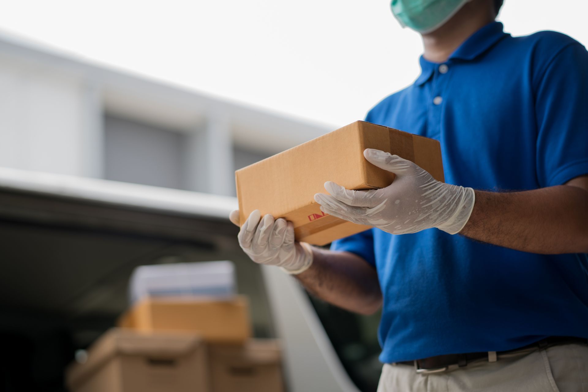 Delivery person in blue shirt, mask, and gloves holding a cardboard box.