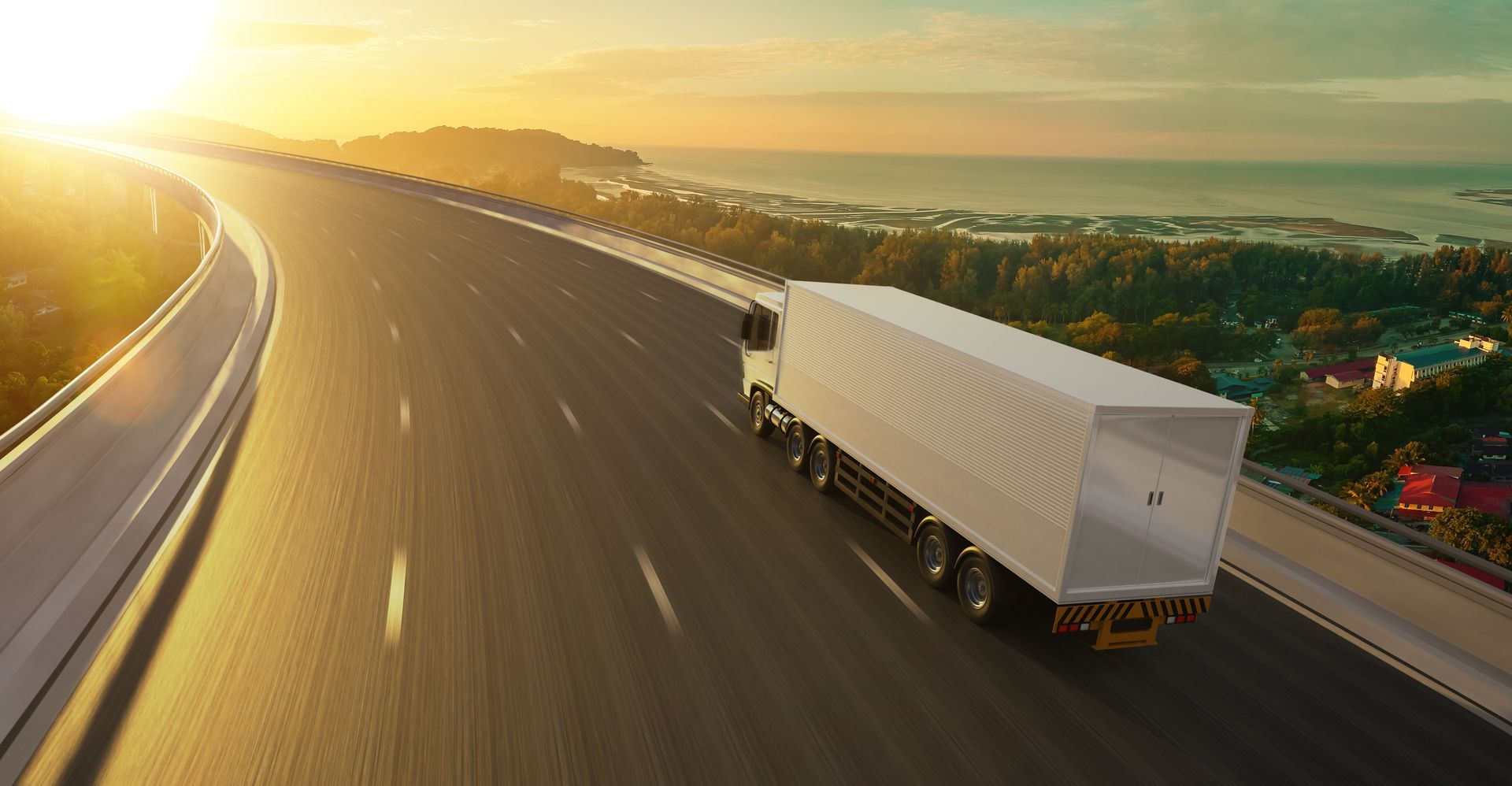 Semi-truck driving on a highway toward the sunrise. Trees and ocean visible in the background.
