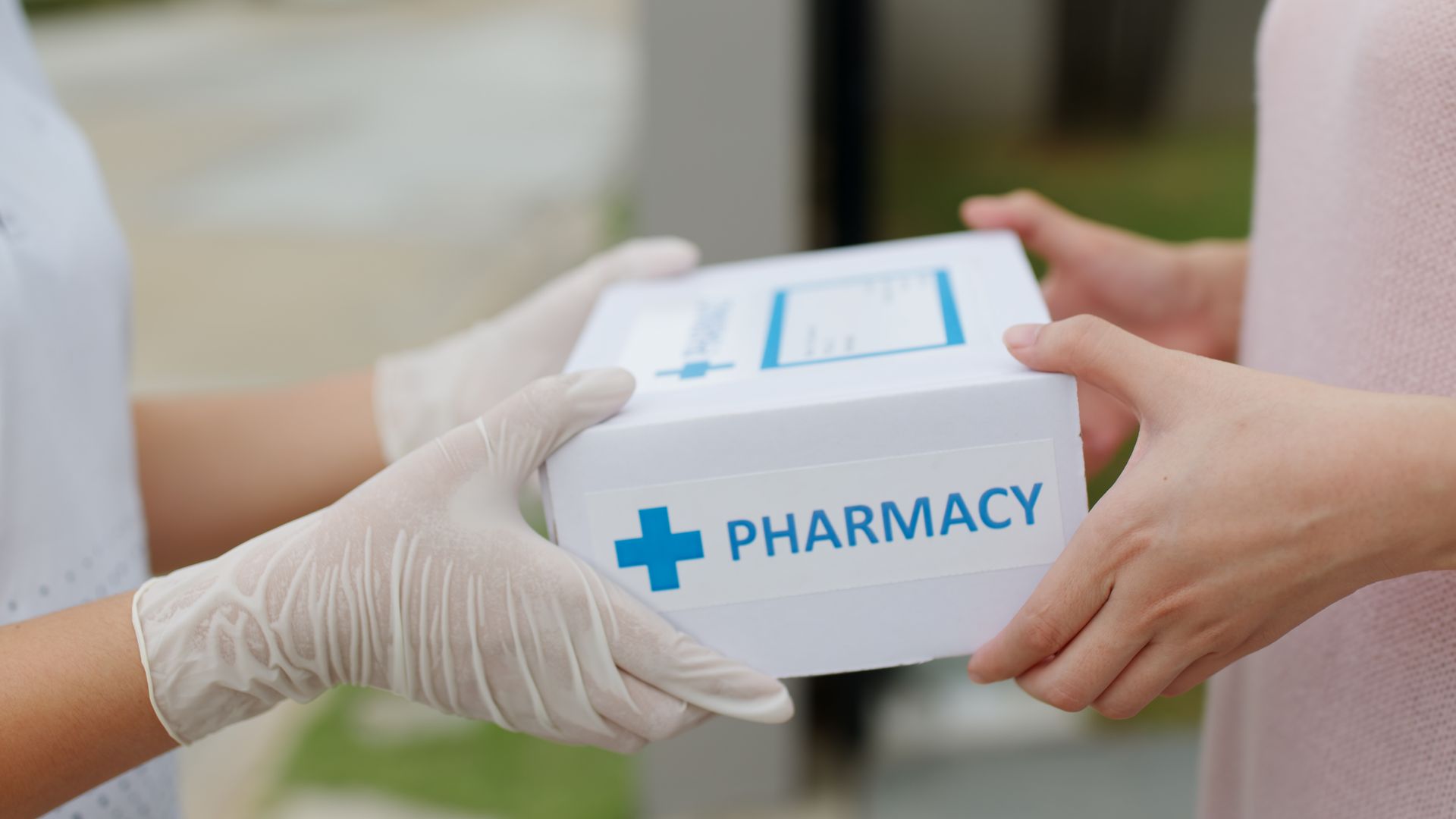 Person in gloves hands a pharmacy box to another person.