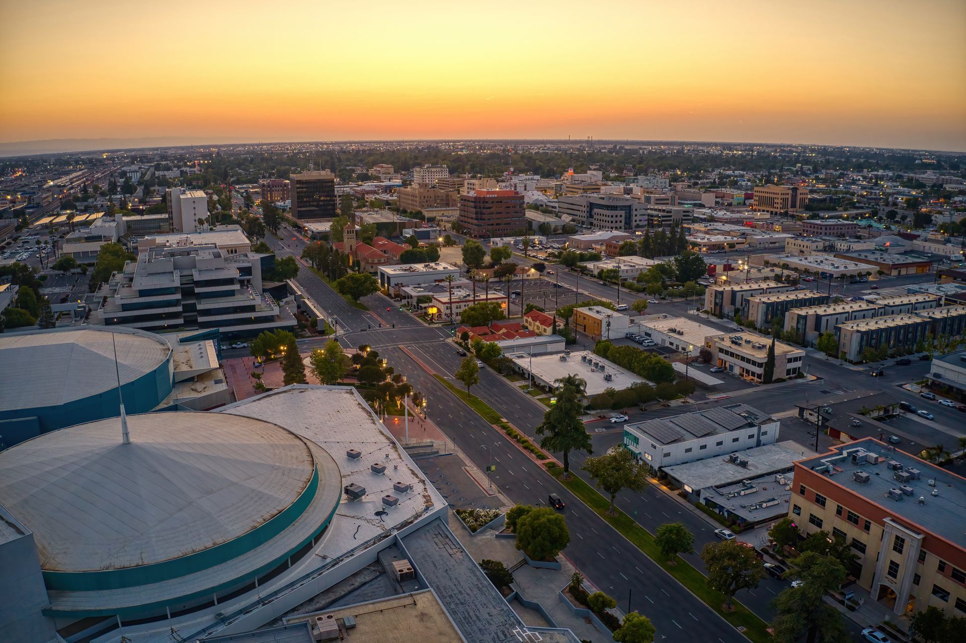 City skyline at dusk with buildings and road under an orange and yellow sky.